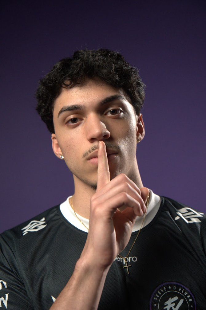 Nuti fazendo sinal de silêncio com o dedo, em fundo roxo